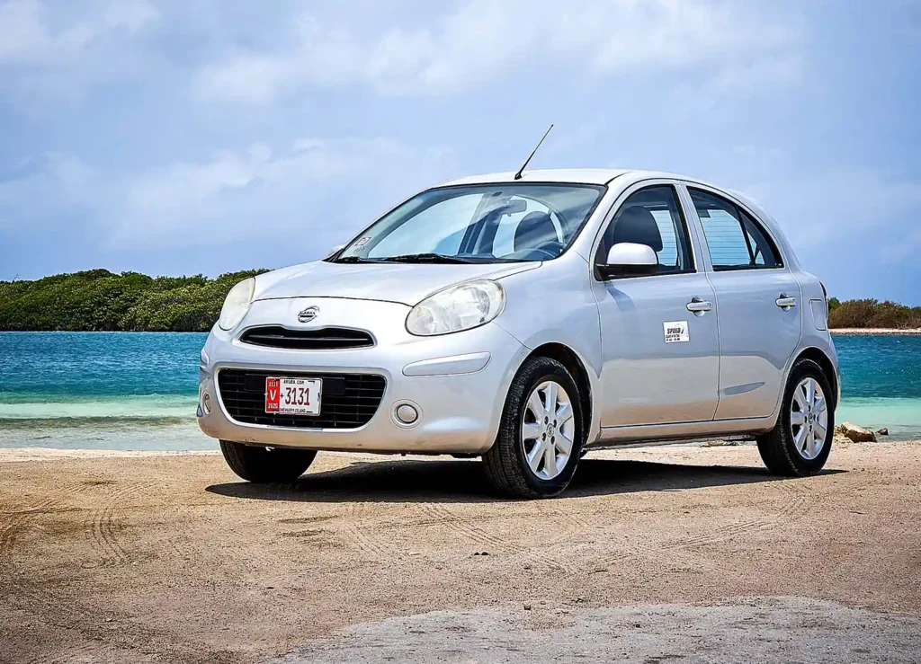 Silver Nissan March rental car parked by the sea in Aruba