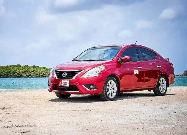 Red Nissan Versa sedan rental parked by the sea in Aruba